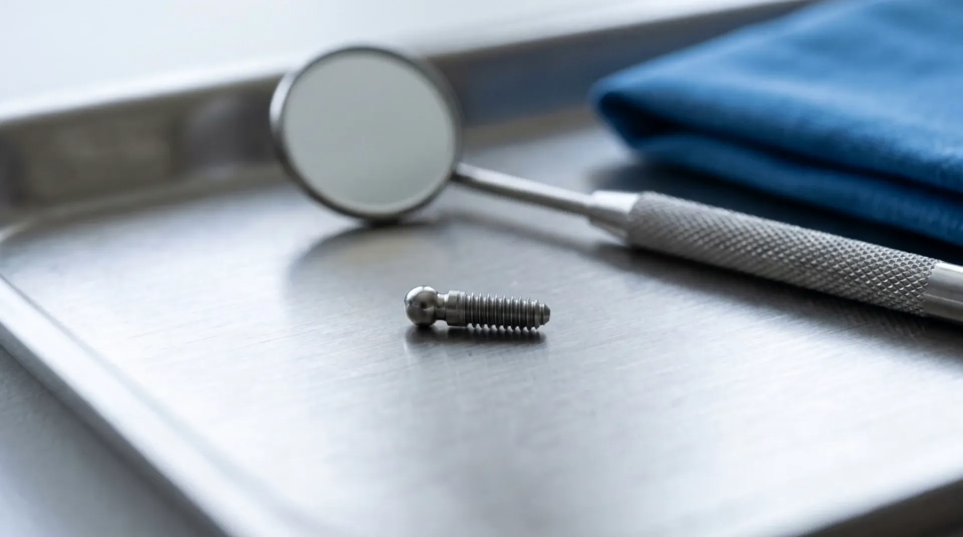 Illustrative macro of a tiny titanium mini dental implant beside a dental mirror and blue cloth
